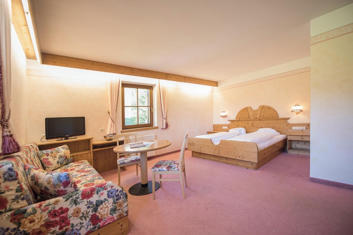 A room with a bed, a television, a table with chairs, and a window.