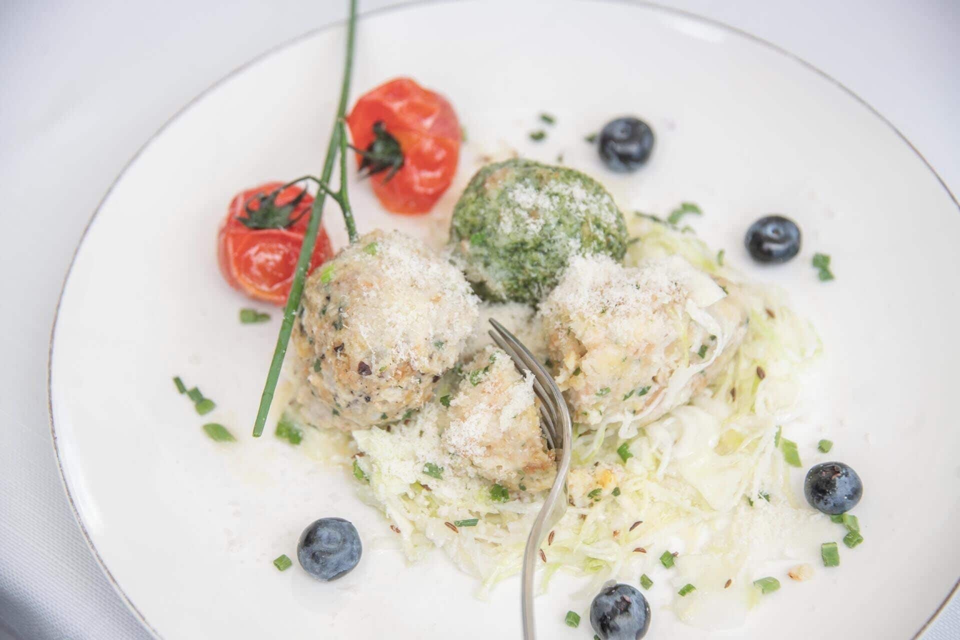 Une assiette contenant divers aliments, notamment des boulettes de viande, une tomate et un légume vert, probablement des brocolis, avec une fourchette.