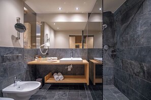 A modern bathroom with a large mirror, a sink, a bidet, and a shower area. - Hotel Edel.Weiss (Trentino-Alto Adige)