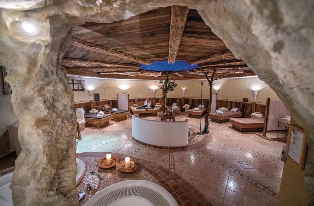 Ein unterirdisches Spa mit Steinwänden, Holzbalken und einer zentralen Lounge mit Kamin.