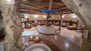 An underground spa with stone walls, wooden beams, and a central seating area with a fire feature.