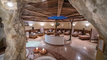 Ein unterirdisches Spa mit Steinwänden, Holzbalken und einer zentralen Lounge mit Kamin.