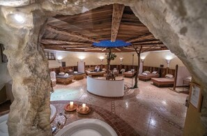 Un spa subterráneo con paredes de piedra, vigas de madera y una zona de estar central con chimenea.