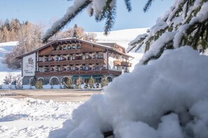 Un hotel de varios pisos con balcones, rodeado de árboles cubiertos de nieve y un cielo despejado.