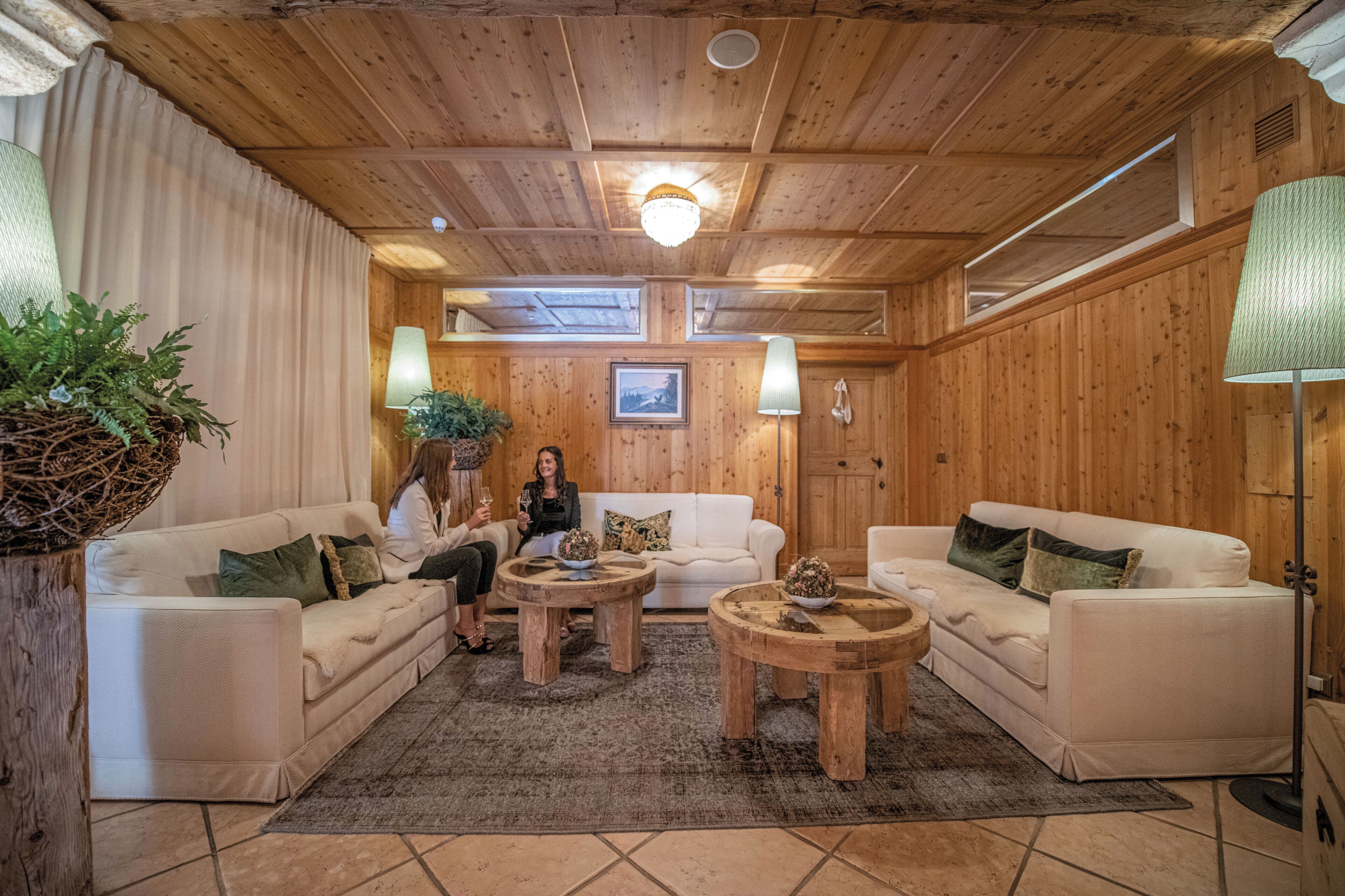 A cozy room with wooden walls, a white sofa, two round wooden tables, and a large window.