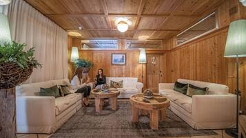 A cozy room with wooden walls, a white sofa, two round wooden tables, and a large window.