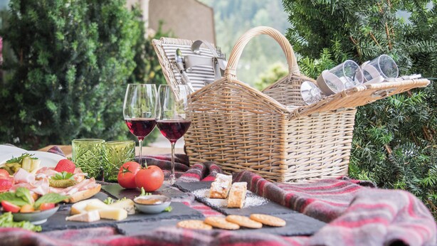 Un montaje para picnic con una cesta de mimbre, copas de vino y diversos alimentos.