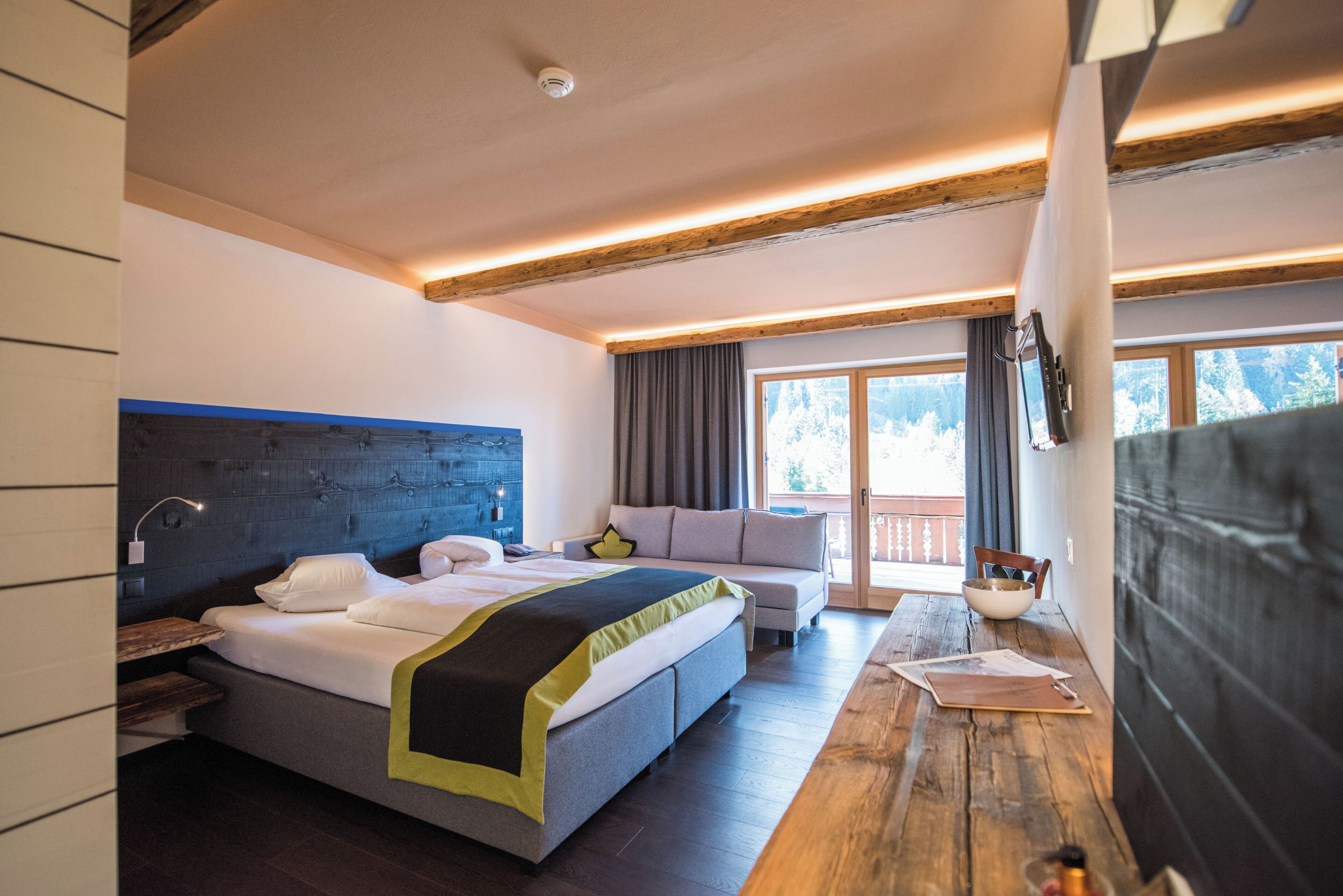 Ein Hotelzimmer mit Bett, Sofa, Esstisch und einem Fenster mit Blick auf Bäume.