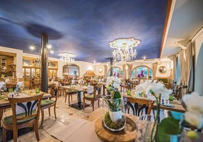A restaurant with multiple dining tables, chairs, and a chandelier. - Hotel Edel.Weiss (Trentino-Alto Adige)