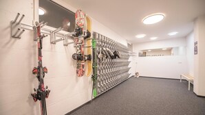A ski storage wall with multiple hooks and a bench in a hallway.