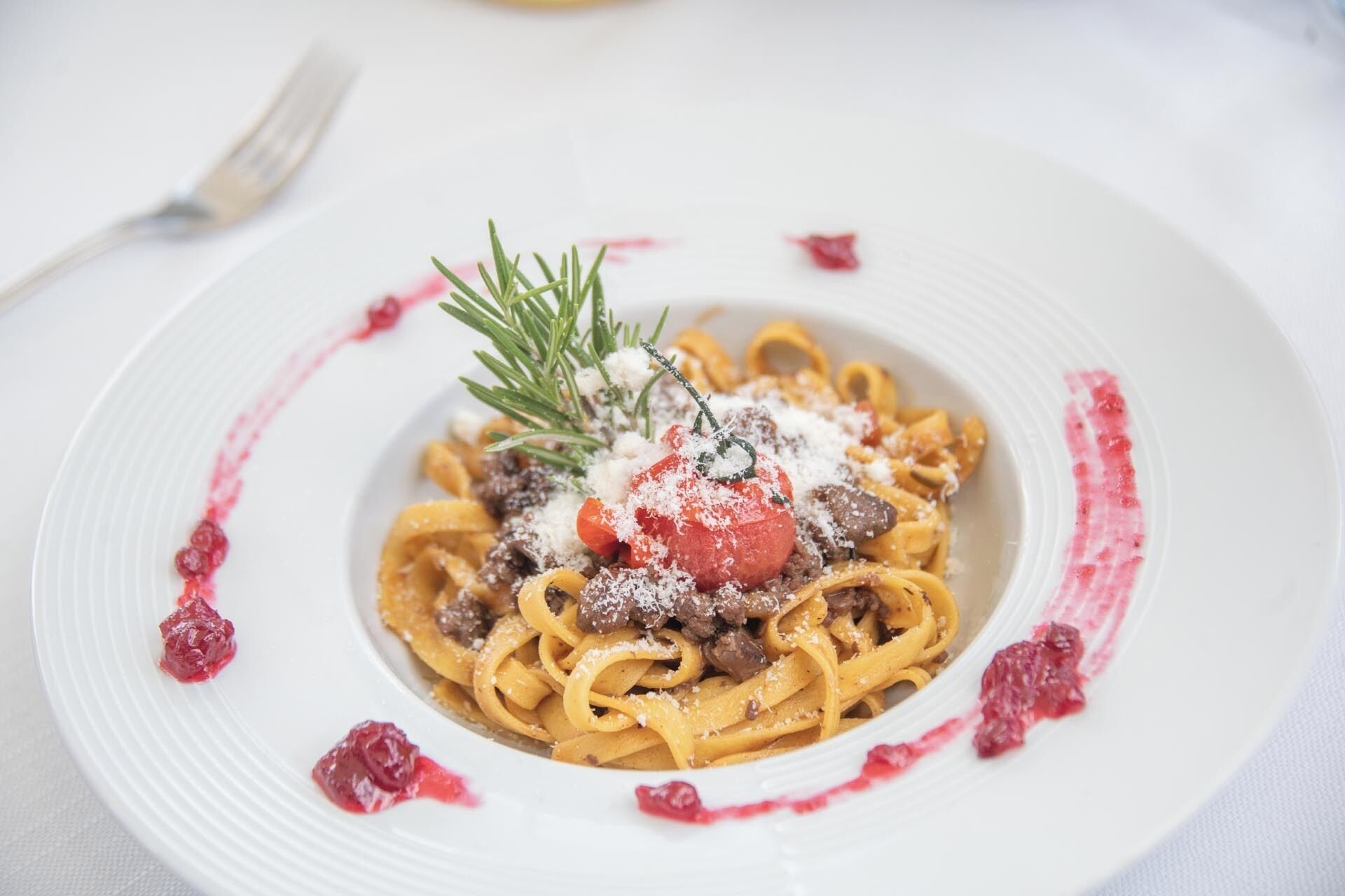 A plate of pasta with a cherry tomato, cheese, and a sprig of rosemary.