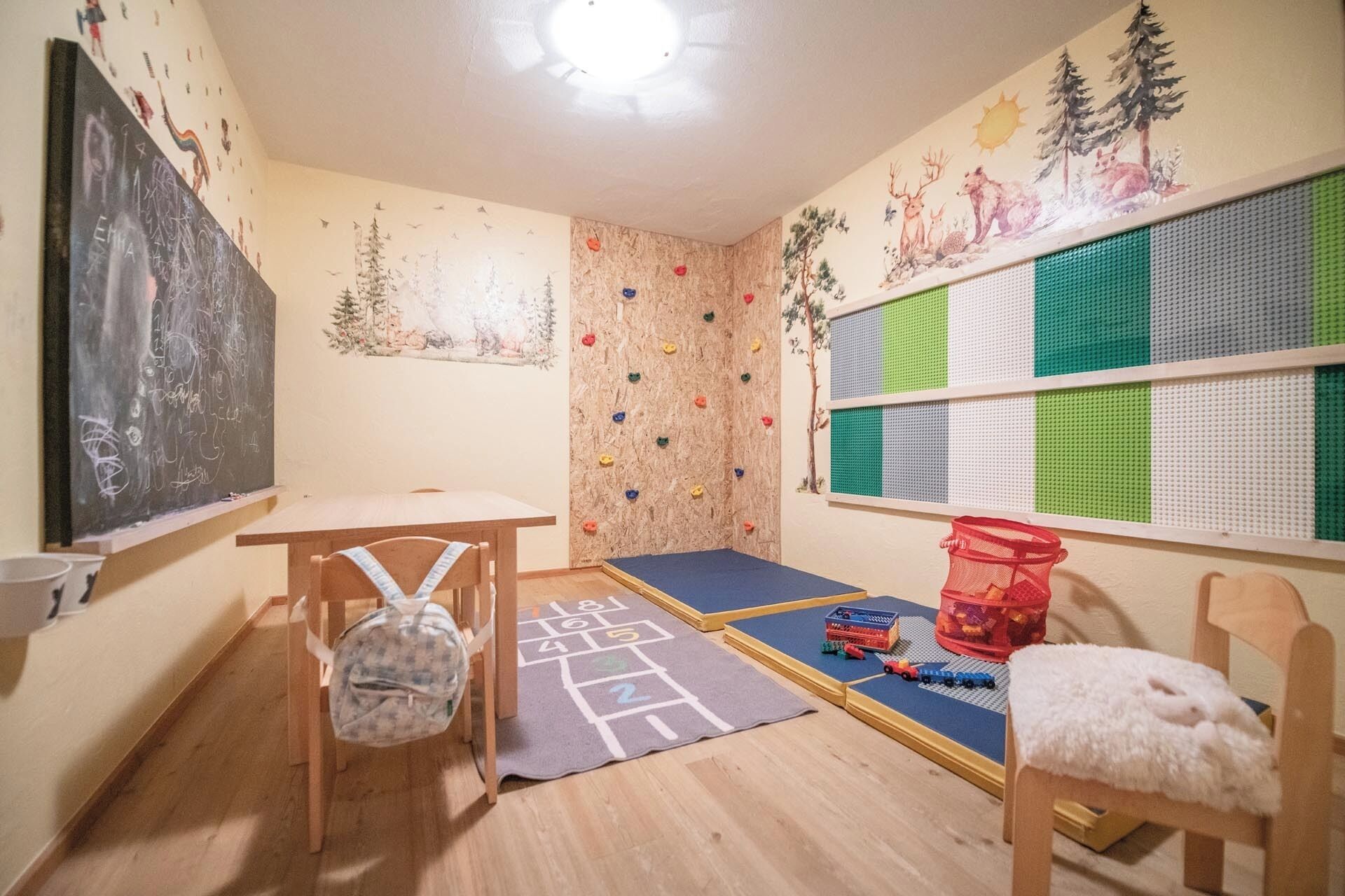 A playroom with a climbing wall, a chalkboard, and a window with a view of trees.