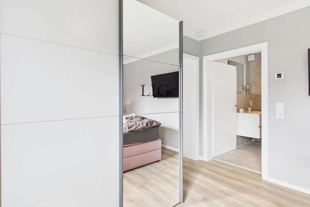A modern hotel room with a mirrored wardrobe, a bed, and a bathroom visible through the mirror.