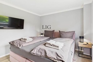 A modern bedroom with a bed, pillows, a nightstand, and a wall-mounted TV. - Erika holiday apartment (Langeoog)