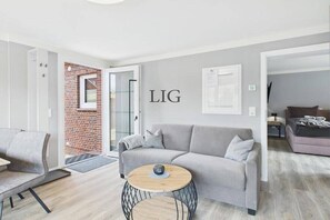 A modern living room with a grey sofa, a round coffee table, and a brick wall. - Erika holiday apartment (Langeoog)