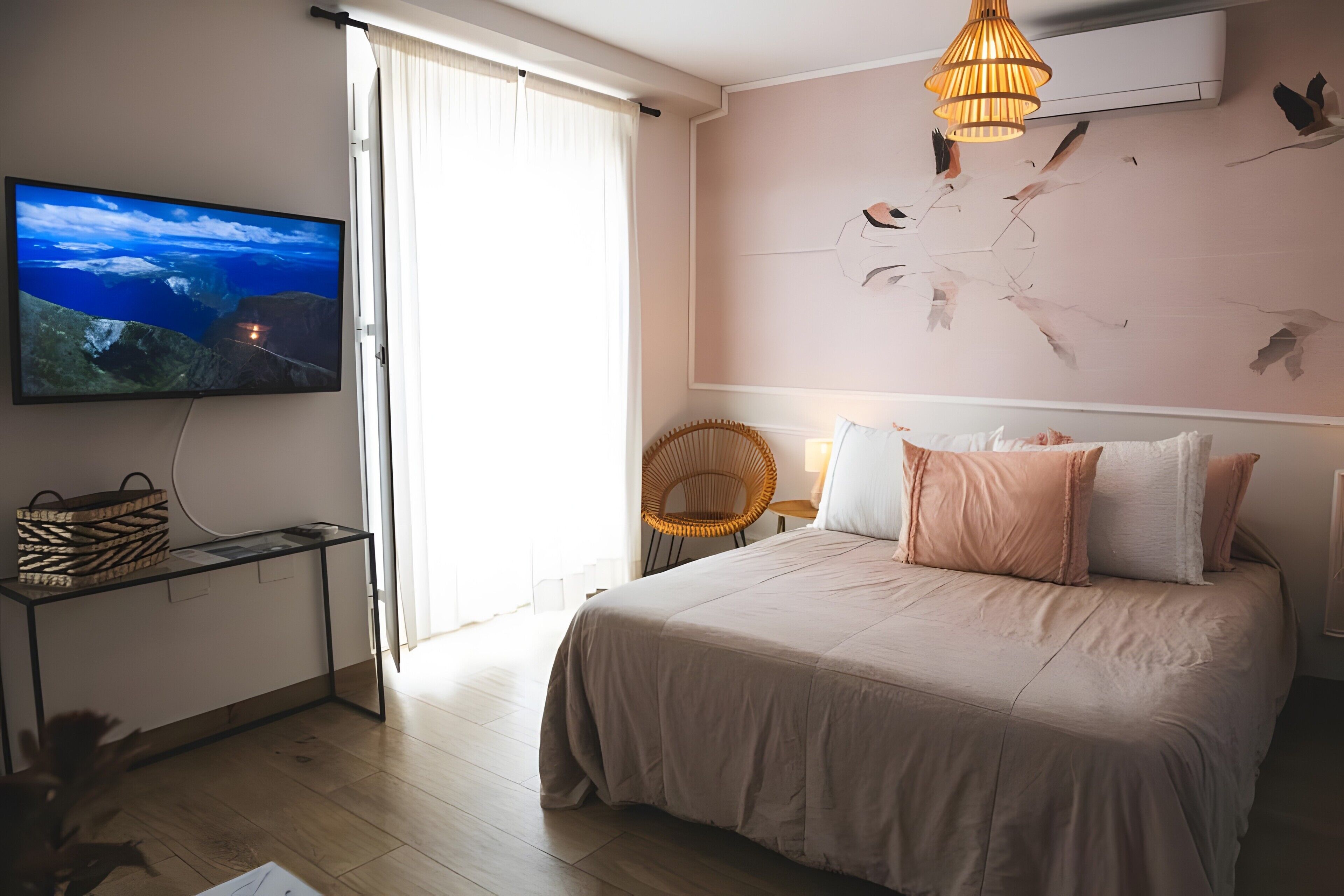 Un dormitorio con cama, televisor en la pared, una silla de mimbre y una lámpara en el techo.