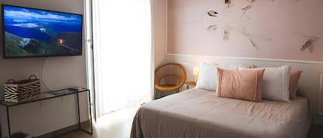 Un dormitorio con cama, televisor en la pared, una silla de mimbre y una lámpara en el techo.