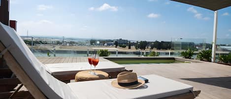 Una terraza en la azotea con sillones de descanso, una mesa con una bebida y vistas panorámicas de la ciudad.
