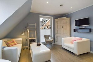 A modern living room with a white sofa, a white armchair, a small white table, a TV mounted on the wall, and a white cabinet. - Holiday apartment in Langeoog with Wi-Fi (Langeoog)