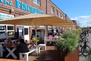 Un espace extérieur aménagé avec des tables et des bancs, un grand parasol et un bâtiment doté d’une enseigne.