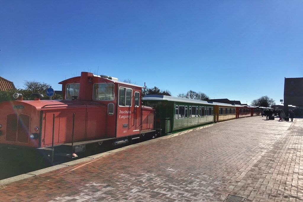 A train station platform with a red train and a green train.