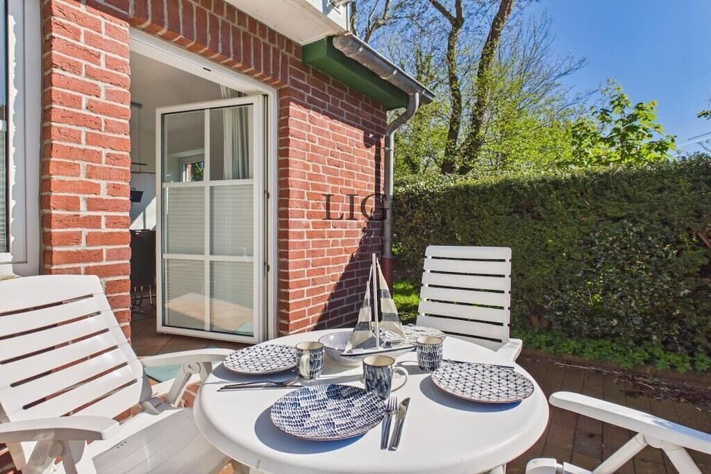 Un espace de restauration en plein air avec une table dressée pour quatre personnes, des chaises blanches et une décoration sur le thème d’un voilier.