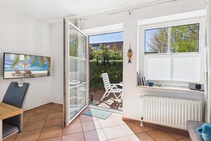 A room with a sliding glass door leading to an outdoor seating area, a dining table with chairs, a radiator, and a wall-mounted TV. - Holiday apartment Island Bliss (Langeoog)