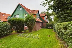 Ein grünes Haus mit rotem Dach, einem gepflegten Rasen und einem Fahrradständer aus Metall.