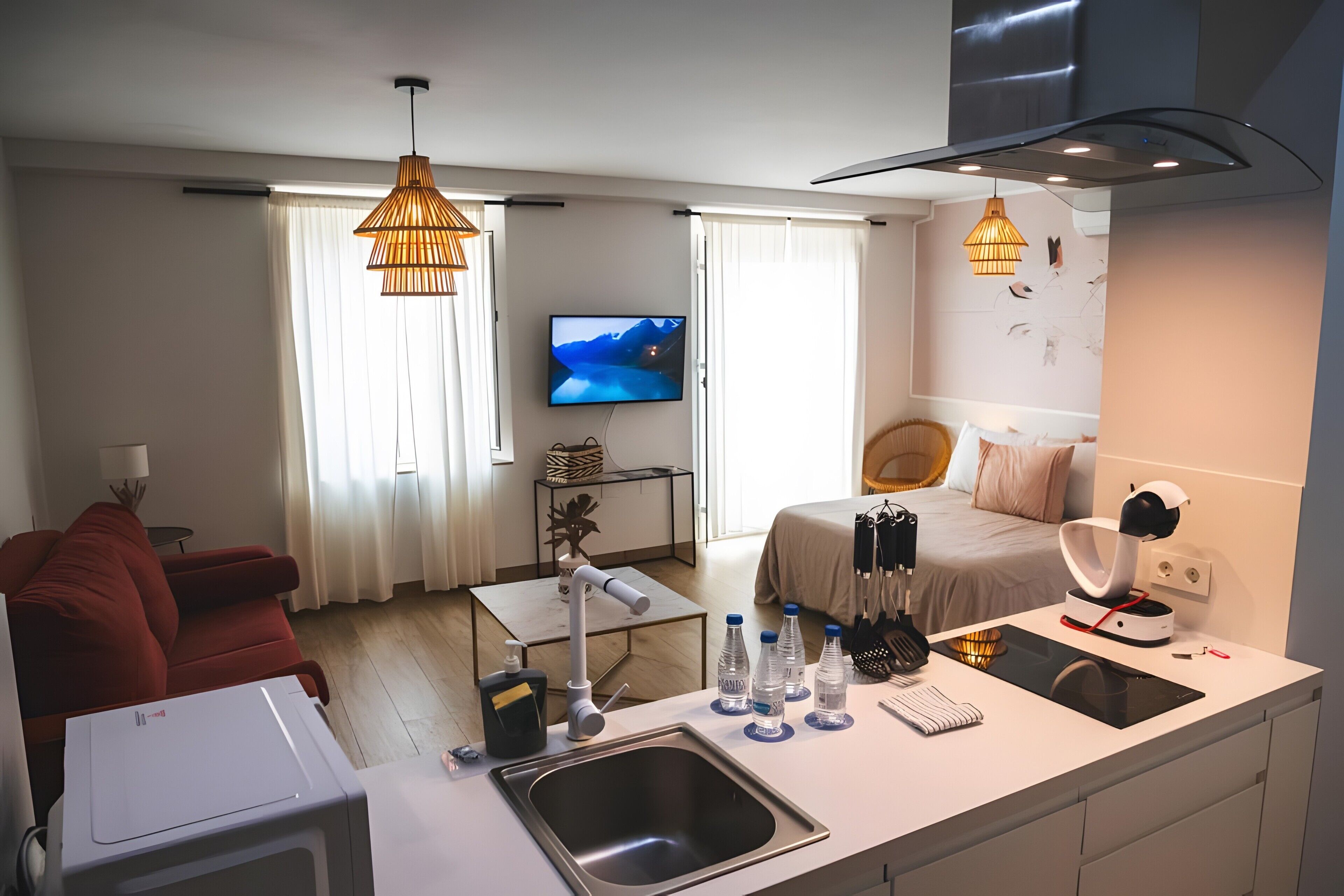 Une chambre d’hôtel moderne dotée d’un coin cuisine, d’une table à manger, d’un canapé rouge, d’une télévision et d’un lit avec une tête de lit.