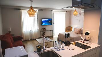Une chambre d’hôtel moderne dotée d’un coin cuisine, d’une table à manger, d’un canapé rouge, d’une télévision et d’un lit avec une tête de lit.