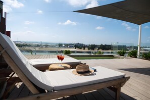 Una terraza en la azotea con sillones de descanso, una mesa con una bebida y vistas panorámicas de la ciudad.