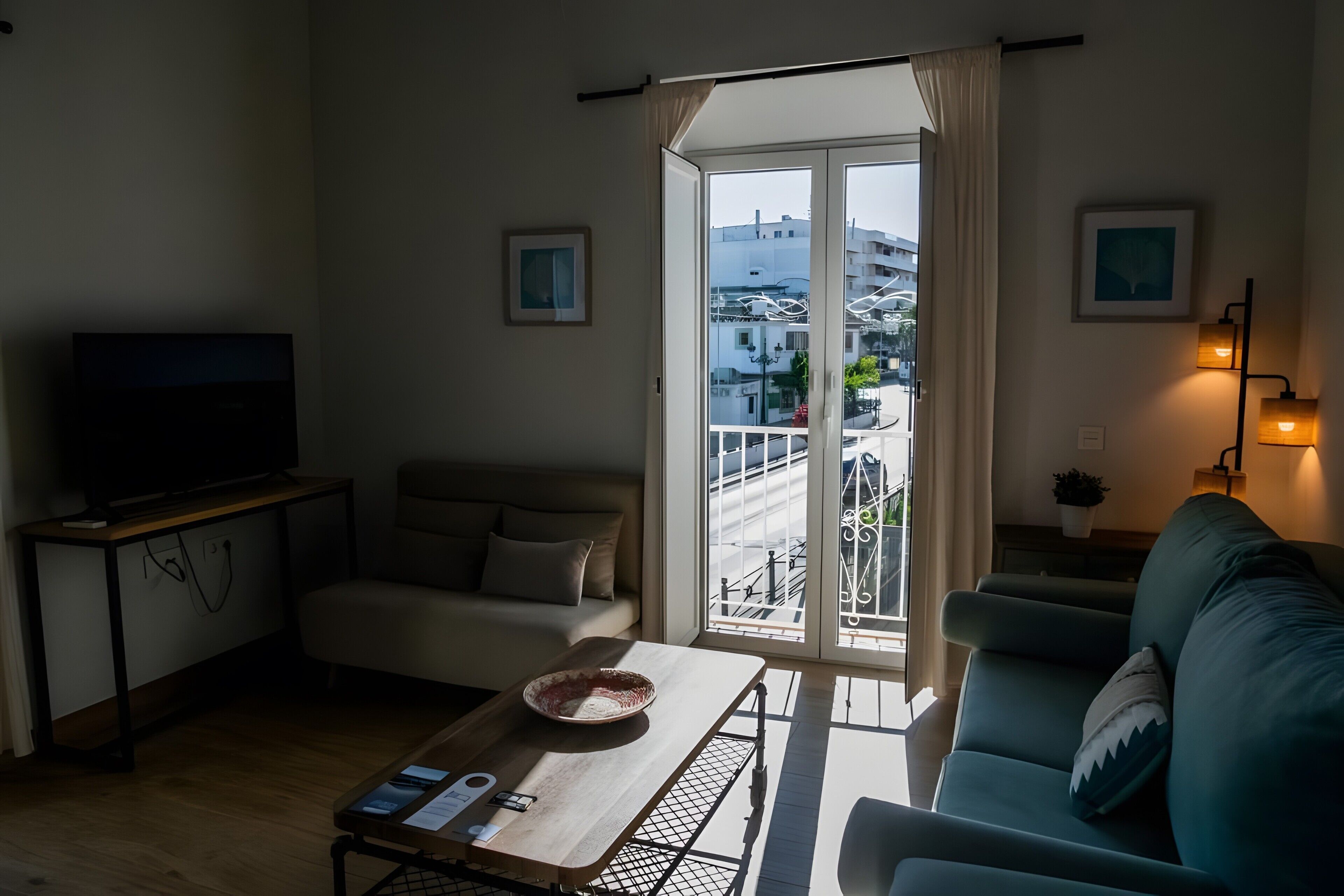 Una sala de estar con un sofá, una mesa de centro con un cuenco y un control remoto, un televisor sobre un mueble bajo, y un balcón con barandilla.