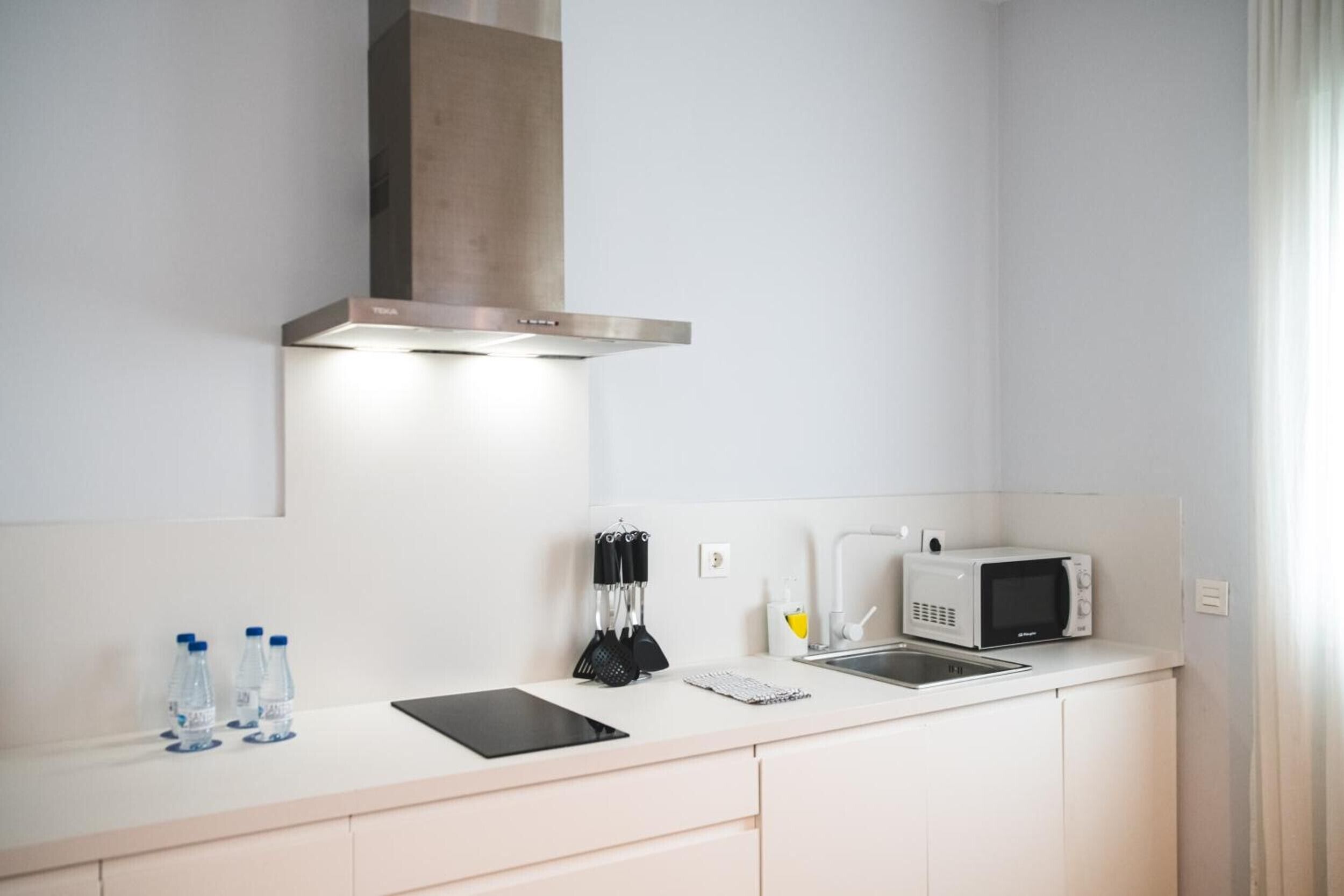 Una cocina moderna con un extractor de acero inoxidable, un microondas y un lavabo.