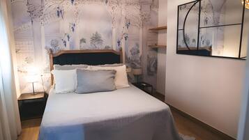 Un dormitorio con una cama, una mesita de noche, una lámpara y una obra de arte colgada en la pared.