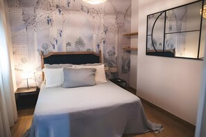 Un dormitorio con una cama, una mesita de noche, una lámpara y una obra de arte colgada en la pared.
