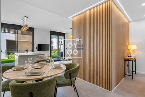 A modern dining area with a round table, green upholstered chairs, and a wooden accent wall. - Santa Rosalía Tropical Garden Corner, pool, lagoon, beach bar, gym by OYOOSTAYS (Torre-Pacheco)