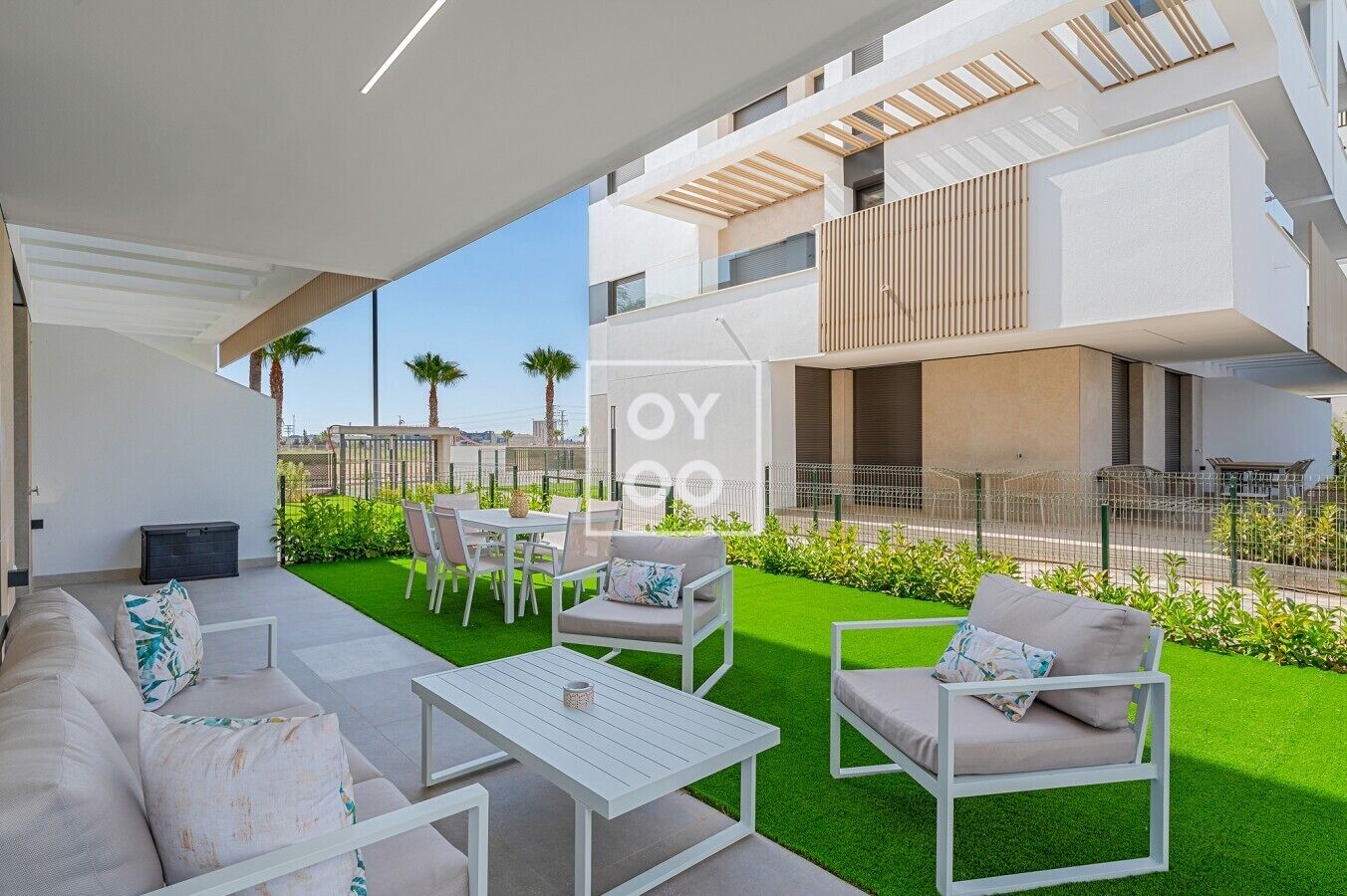 An outdoor patio area with a white sofa, chairs, and a table, surrounded by artificial green grass.