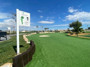 Een golfbaan met een bordje waarop staat: hole 1, een par 3, afstand 20 meter.