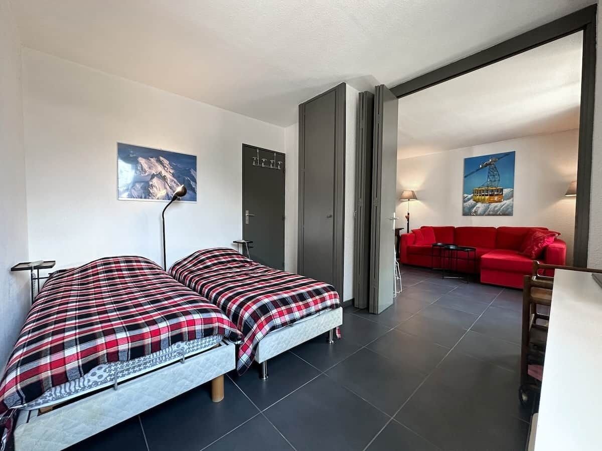 A bedroom with two beds, a red sofa, and a dining area.