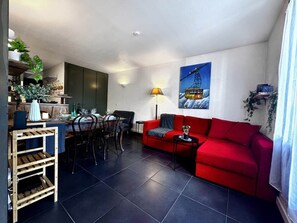 A modern living room with a red sofa, dining area, and kitchen. - La Vue Blanche – Spacious, Balcony & Mont Blanc View (Chamonix)