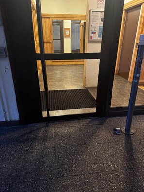 A hotel entrance with a metal barrier, a textured wall, and a door with a wooden frame. - La Vue Blanche – Spacious, Balcony & Mont Blanc View (Chamonix)
