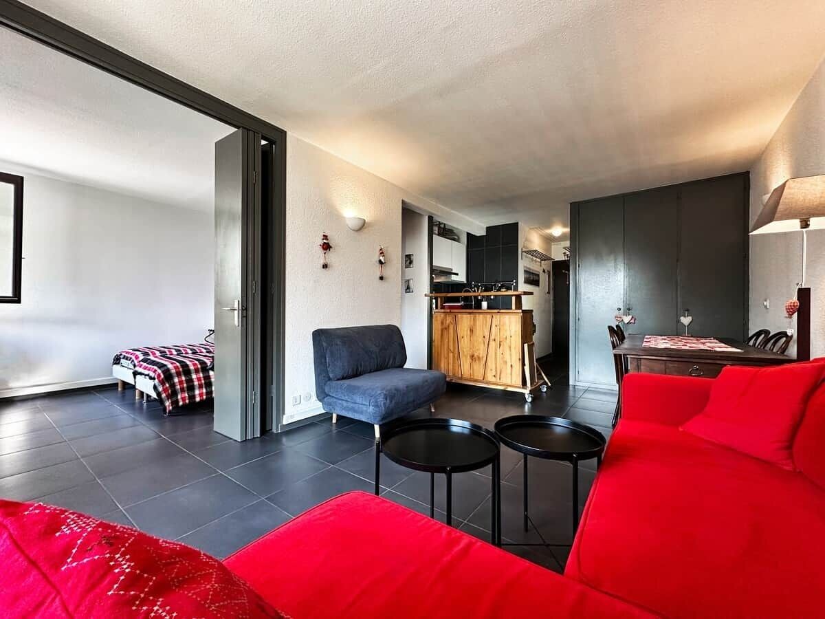 Un soggiorno moderno con un divano rosso, una poltrona blu e un'area pranzo con un mobiletto in legno e un tavolo.