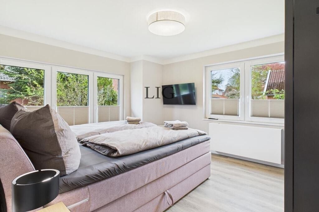 A modern bedroom with a bed, a TV, and large windows.