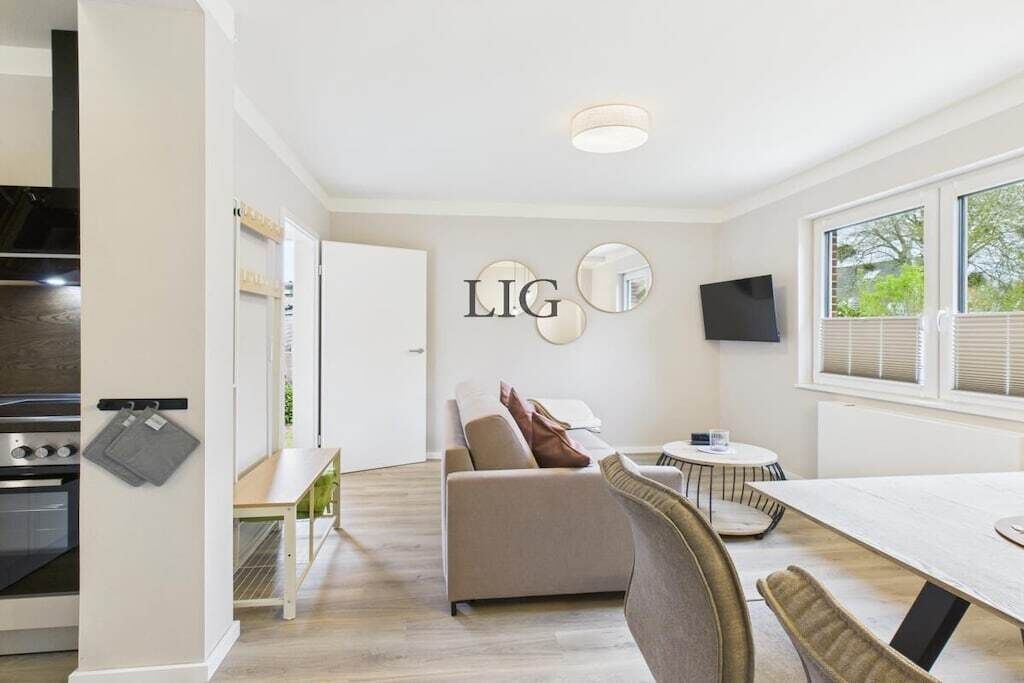 A modern kitchen with a built-in oven, a dining area with a table and chairs, and a living space with a sofa and a TV.