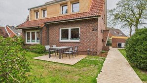 Een tweelaags huis met een bakstenen gevel, een houten terras en een patio met een tafel en stoelen.