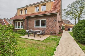 Ein zweistöckiges Haus mit Backsteinfassade, einer Holzterrasse und einer Terrasse mit Tisch und Stühlen.