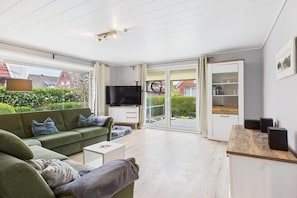 A modern living room with a sofa, coffee table, and a TV. There is a sliding glass door leading to a balcony. - Holiday apartment Strandkoje (Langeoog)