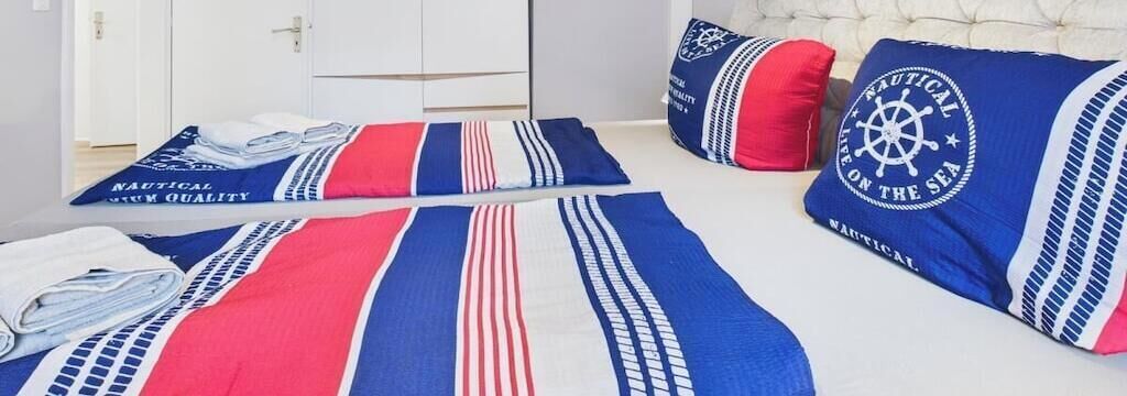 Ein Bett mit marineblauer Bettwäsche und Kissen, ein ordentlich gefaltetes weißes Handtuch und ein weißer Kopfteil.