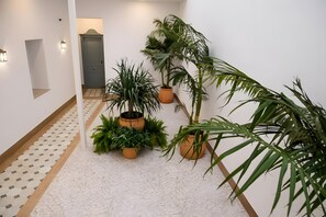 Um corredor com piso ladrilhado, um banco de madeira e vários vasos com plantas.