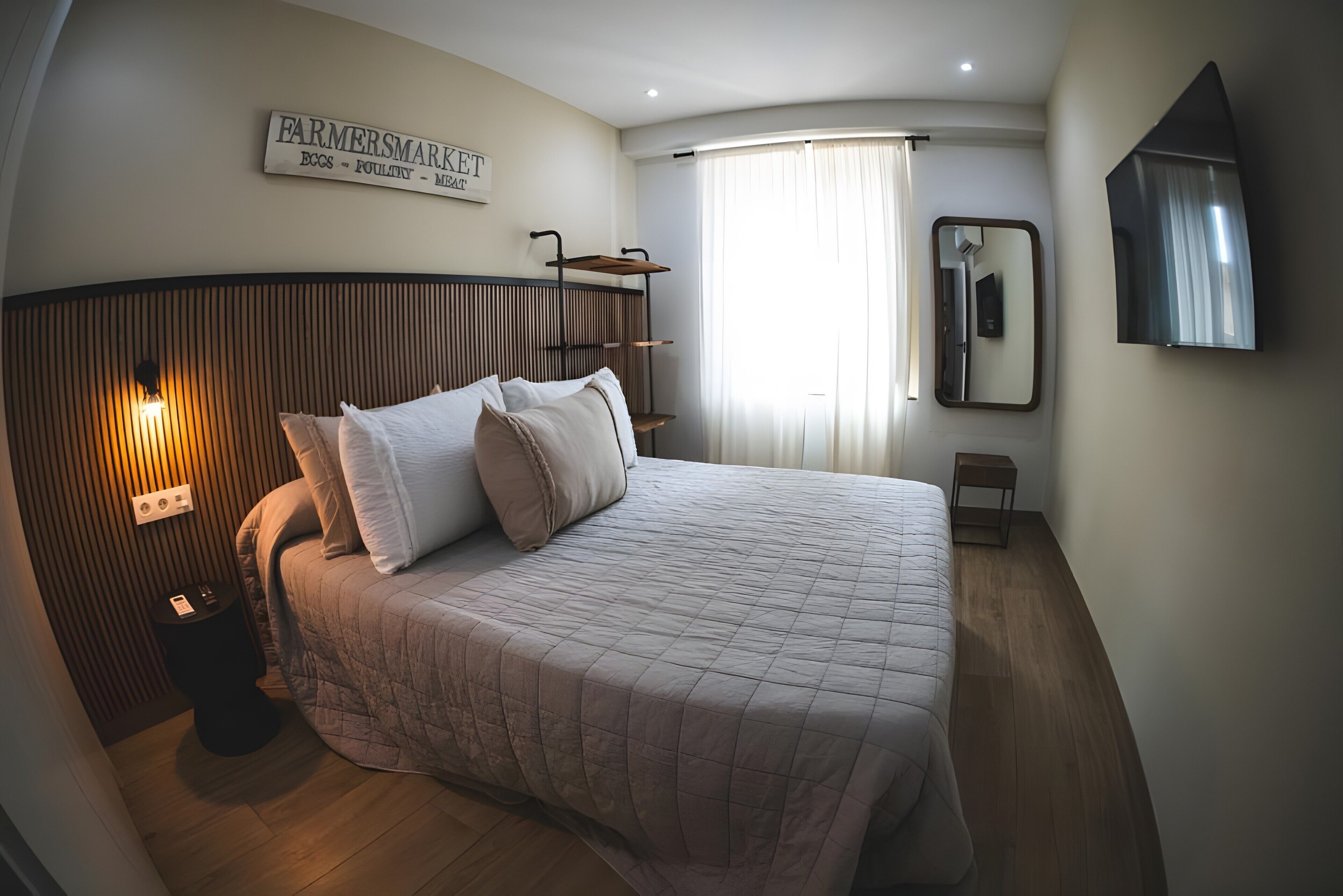 Quarto com cama, luminárias de cabeceira, mesa de apoio, espelho e uma placa na parede.
